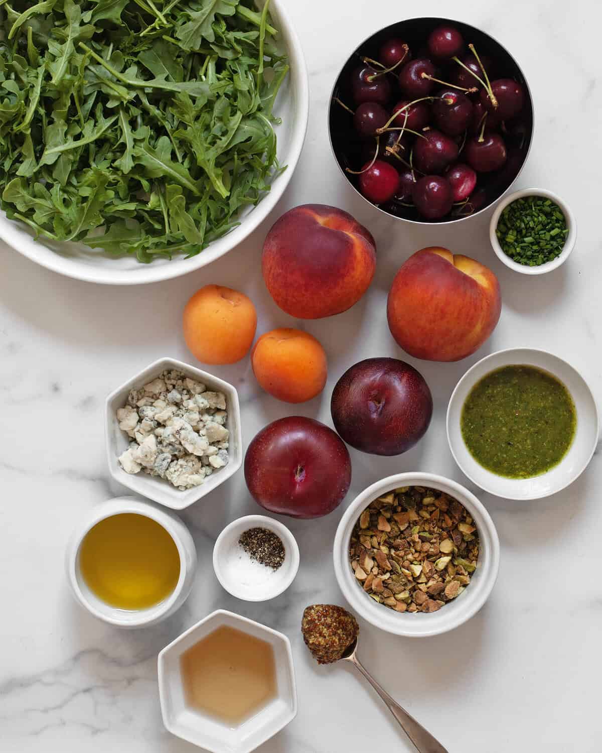 Ingredients including peaches, apricots, plums, cherries, arugula, gorgonzola, pistachios, chives, pesto. white wine vinegar, olive oil, salt and pepper.