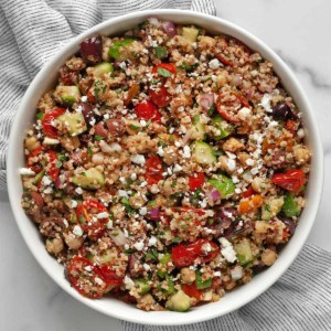 Quinoa salad with chickpeas, roasted tomatoes, cucumber, olives and feta in a large bowl.