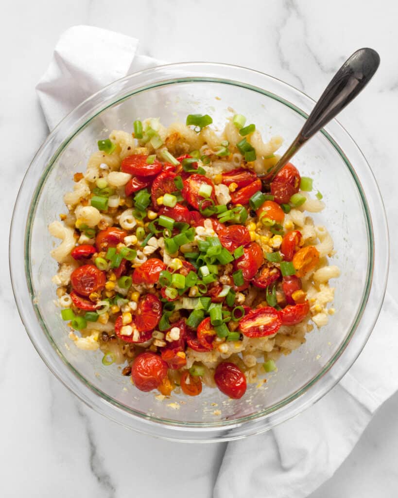 Stirring tomatoes, corn and scallions into pasta