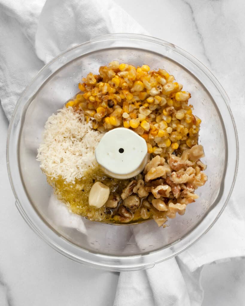 Roasted corn, parmesan, walnuts, garlic, olive oil and lemon juice in a bowl for pesto