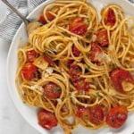 Spaghetti with burst cherry tomatoes on a plate.