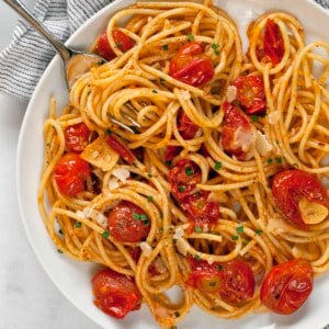 Spaghetti with burst cherry tomatoes on a plate.