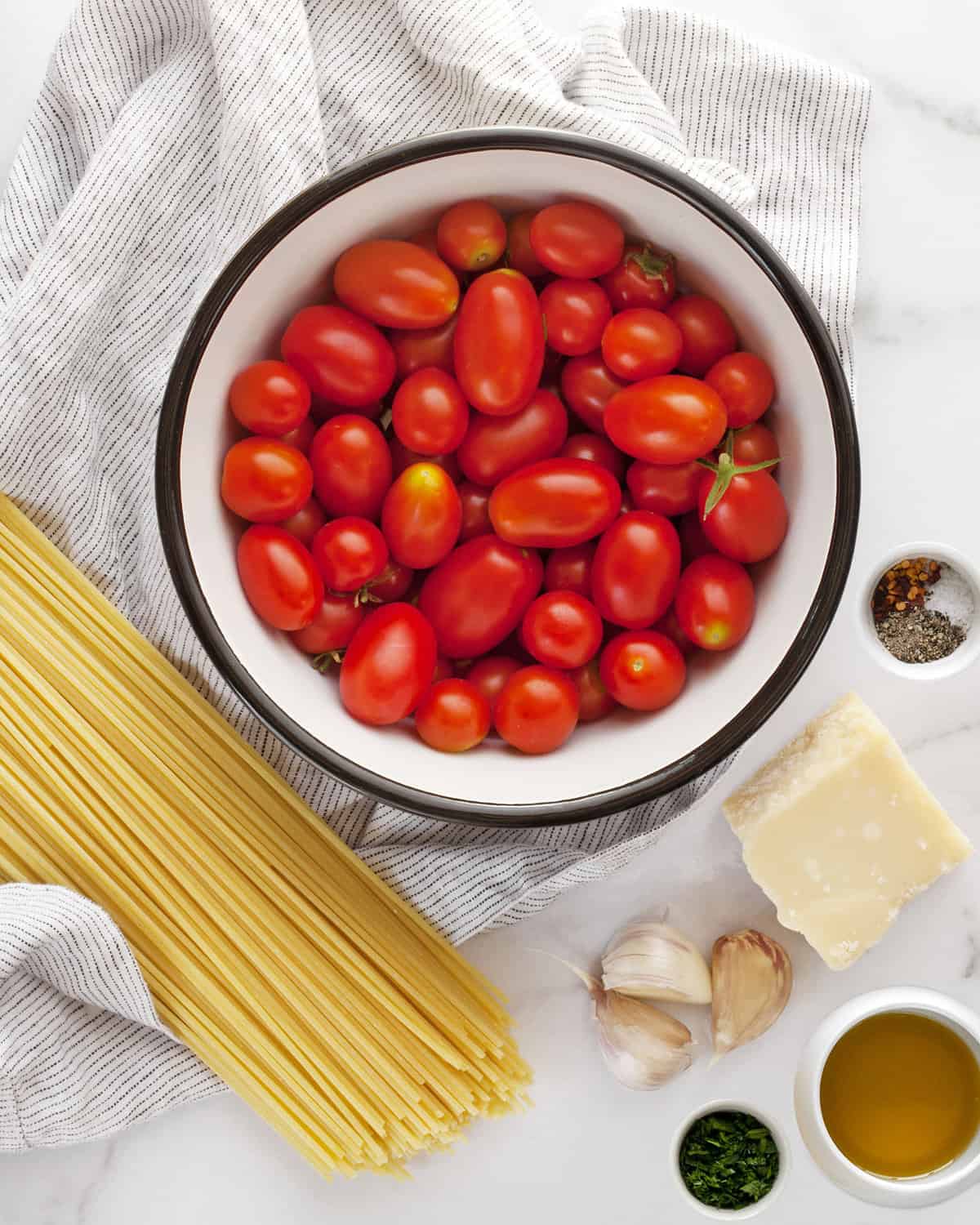 Ingredients including spaghetti, tomatoes, garlic, spices, olive oil, parmesan and fresh herbs.