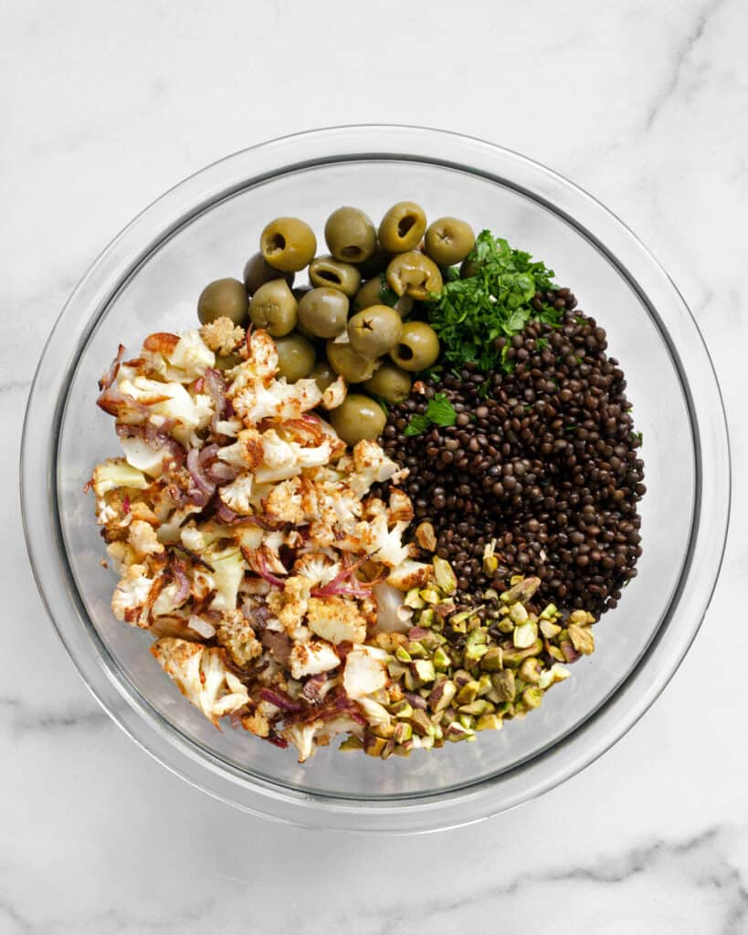 Combining cauliflower, onions, lentils, olives, pistachios and parsley in a bowl