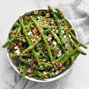 Roasted green beans topped with breadcrumbs and almonds in a bowl.