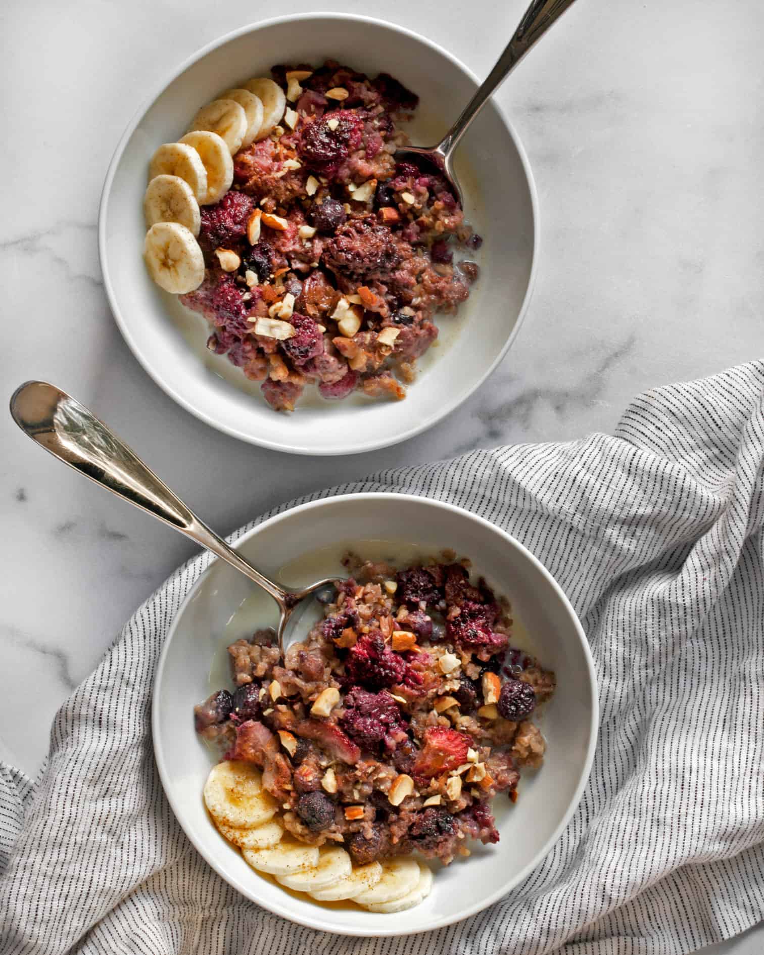 Berry baked steel-cut oatmeal in two bowls topped with bananas