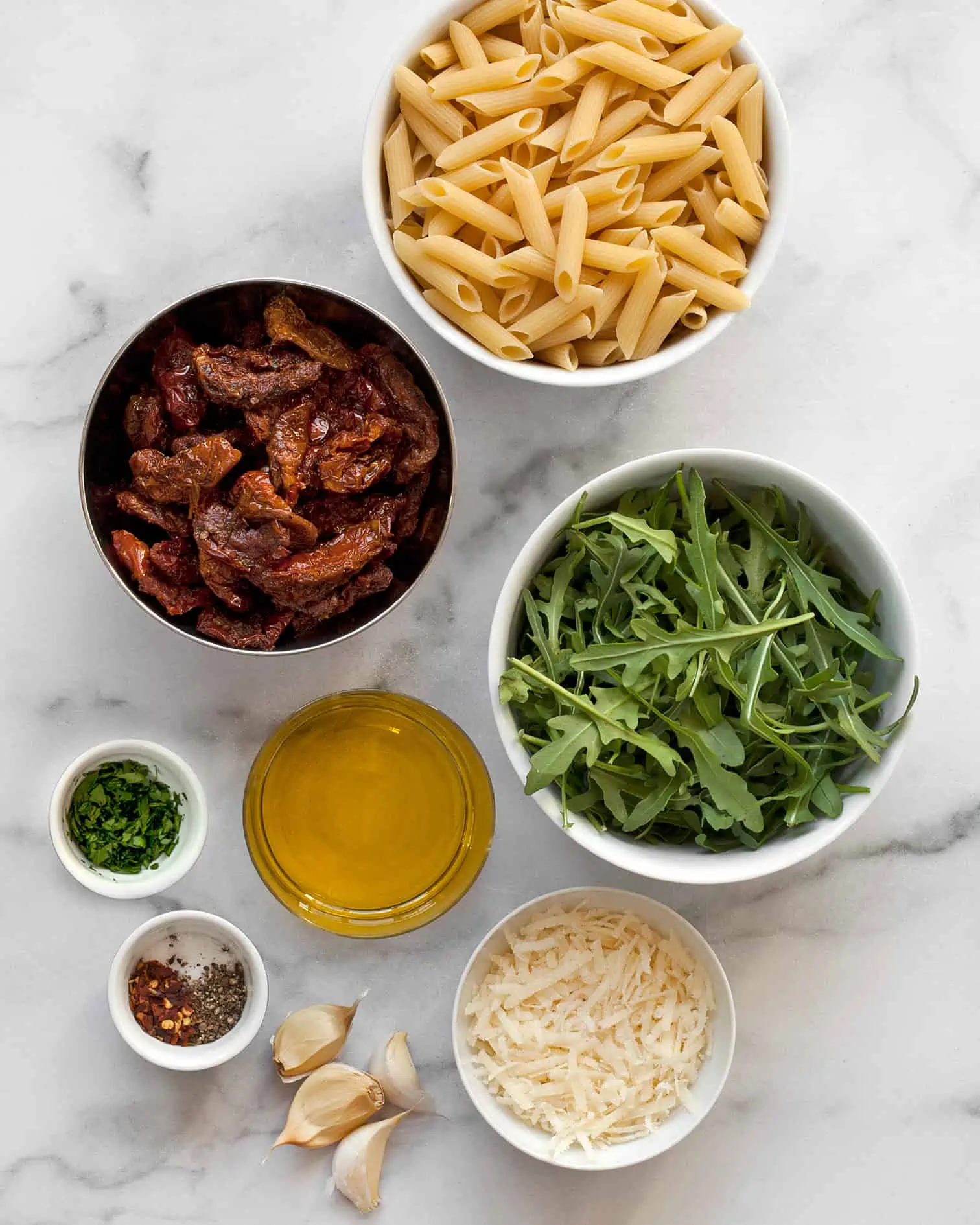 Ingredients including penne, sun dried tomatoes, arugula, olive oil, garlic and parmesan