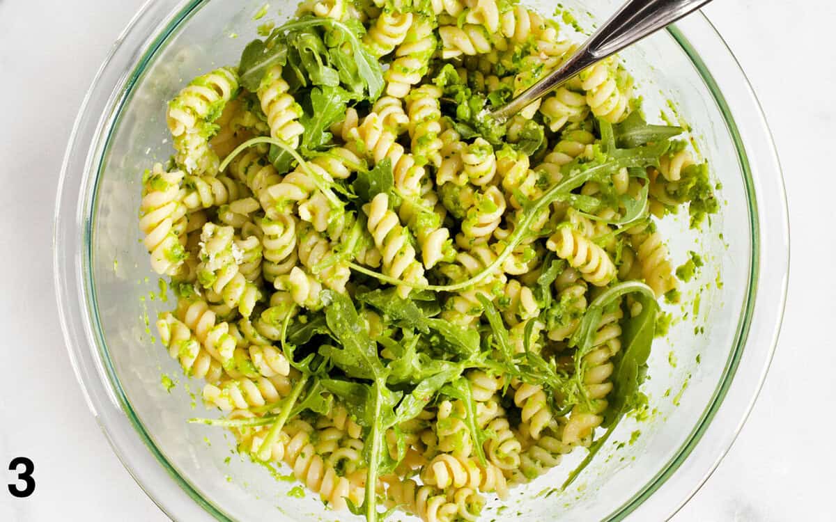 Rotini pasta tossed with pea pesto, arugula and parmesan in a bowl.