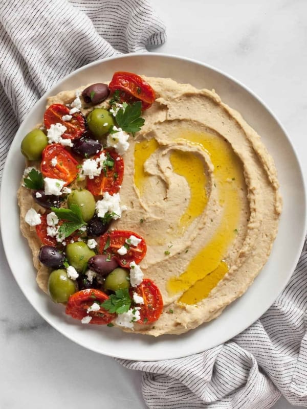 Roasted garlic hummus topped with roasted tomatoes, olives and feta spread on a plate.