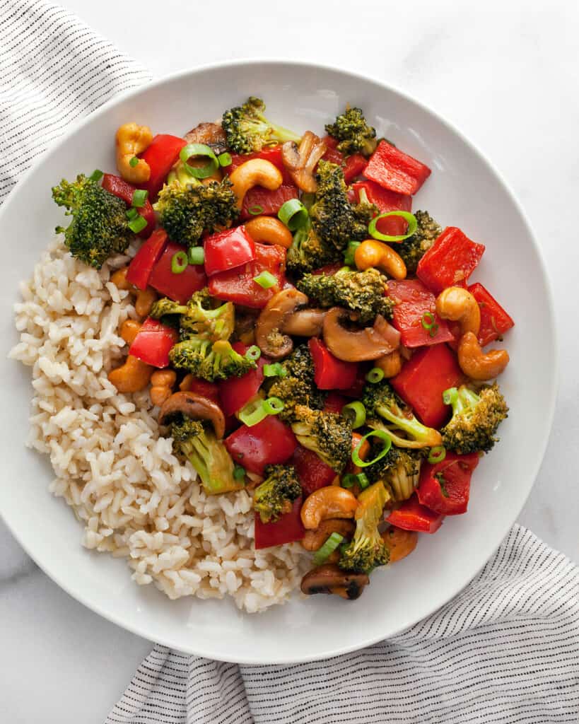 Veggie stir-fry with cashews and rice on a plate.