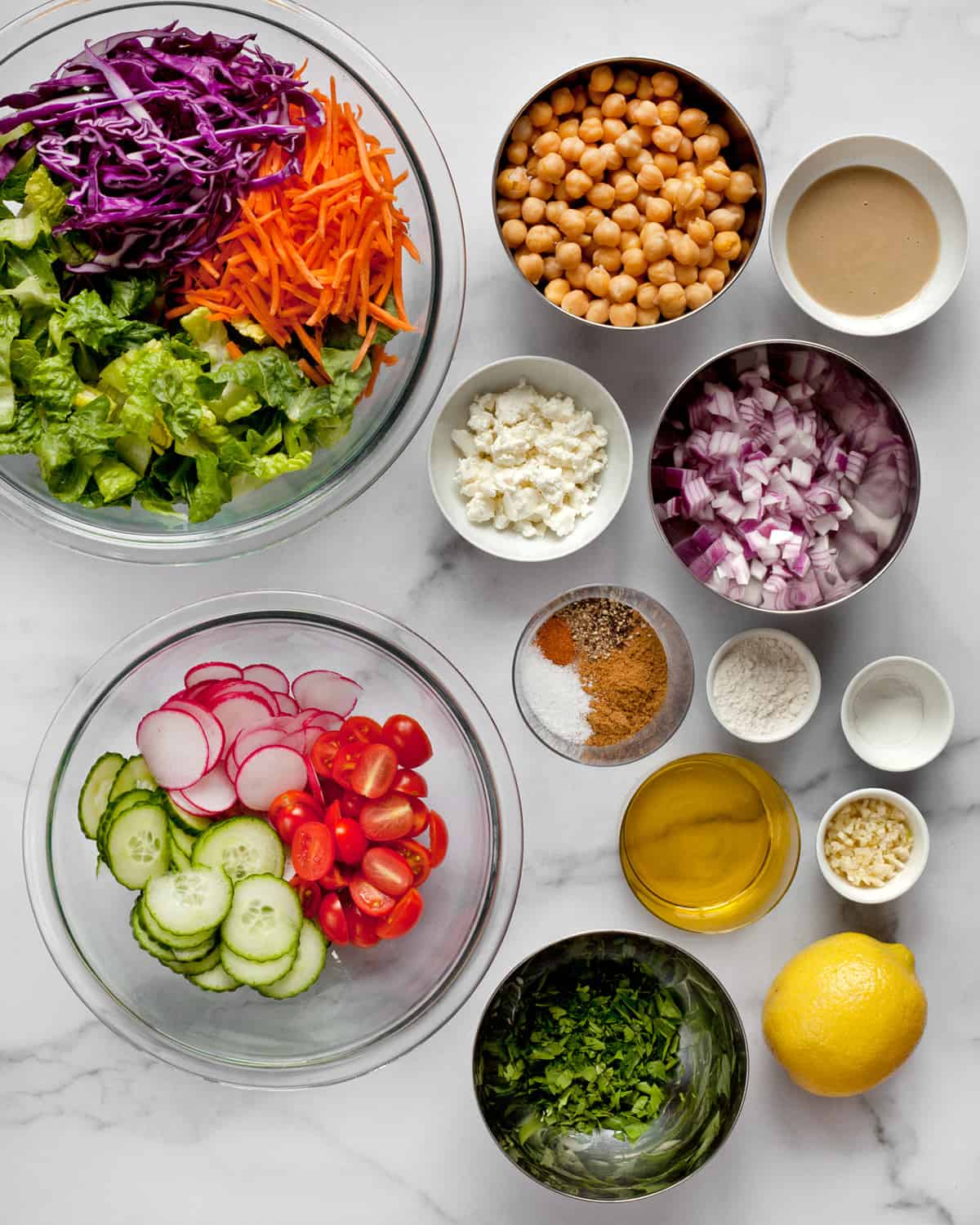 Ingredients including chickpeas, romaine, carrots, cabbage, cucumbers, tomatoes radishes and spices.