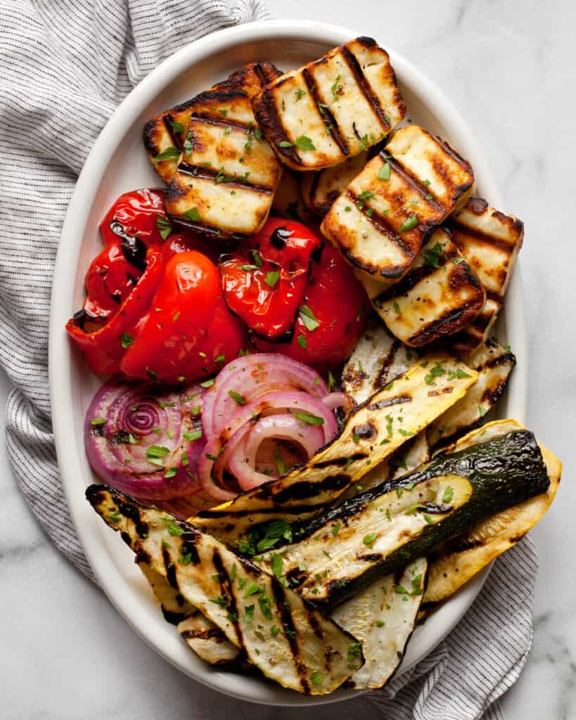 Grilled halloumi with grilled vegetables on an oval serving dish.