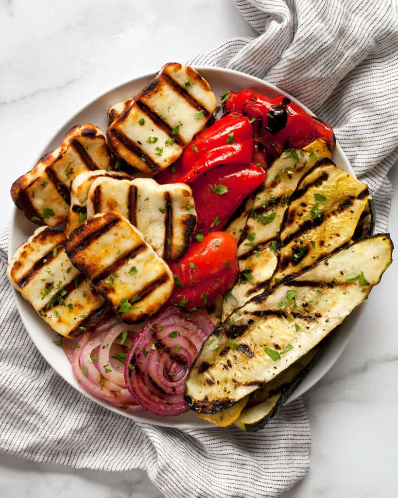 Grilled halloumi cheese with grill marks and grilled zucchini, squash, pepeprs and onions.