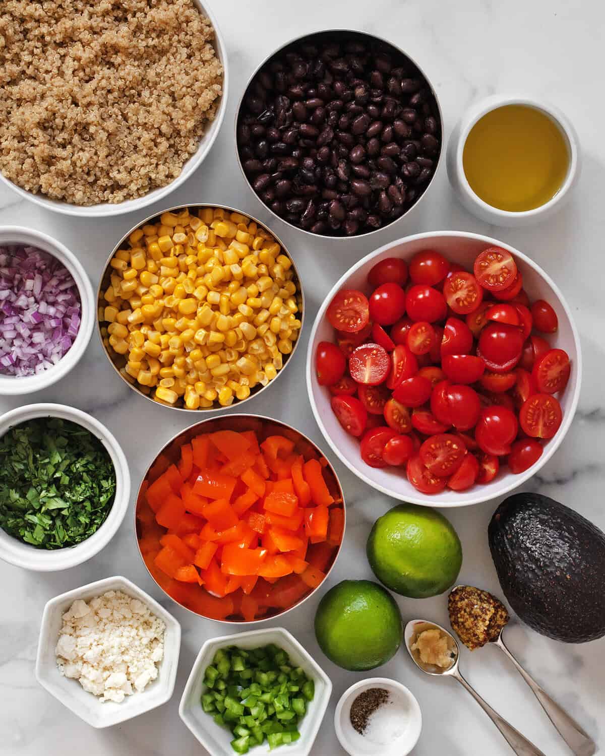 Ingredients including black beans, cooked quinoa, corn, tomatoes, peppers, red onions, jalapenos, limes, feta, avocado, garlic, mustard, olive oil, salt and pepper