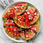 Grilled watermelon slices on a plate with feta and basil.