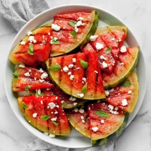 Grilled watermelon slices on a plate with feta and basil.