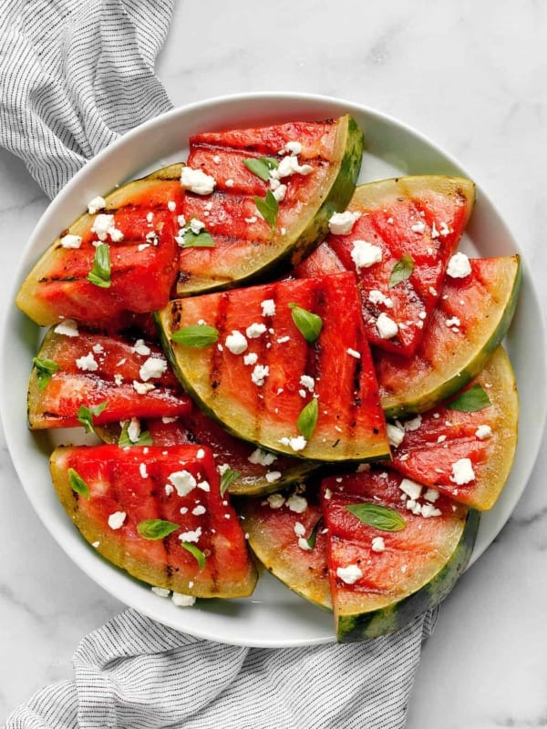 Grilled watermelon slices on a plate with feta and basil.