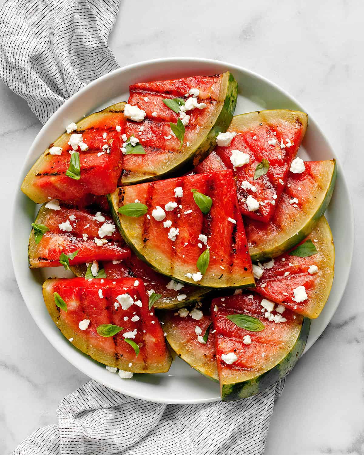 Grilled watermelon slices on a plate with feta and basil.