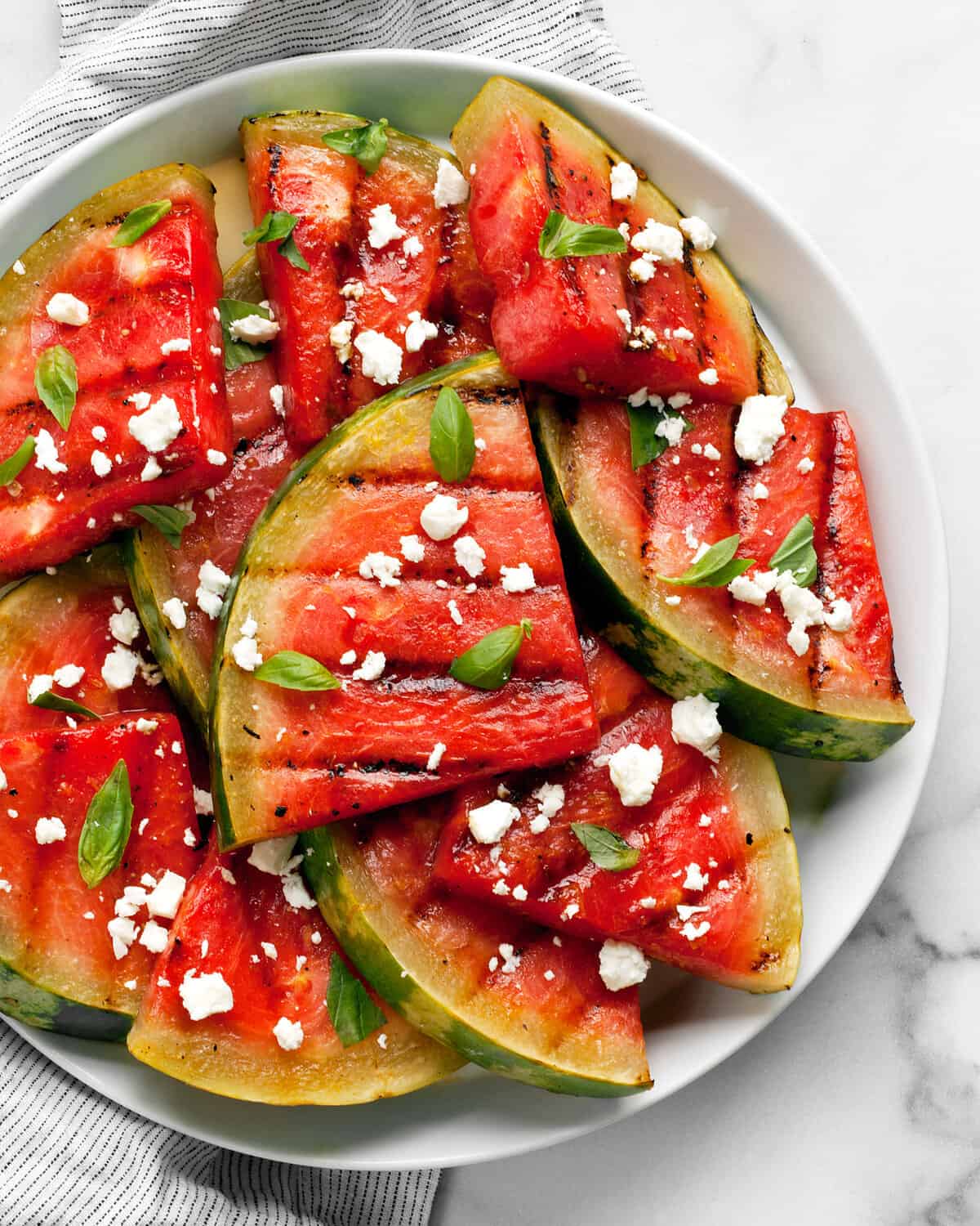 Grilled watermelon wedges with feta and basil on a plate.