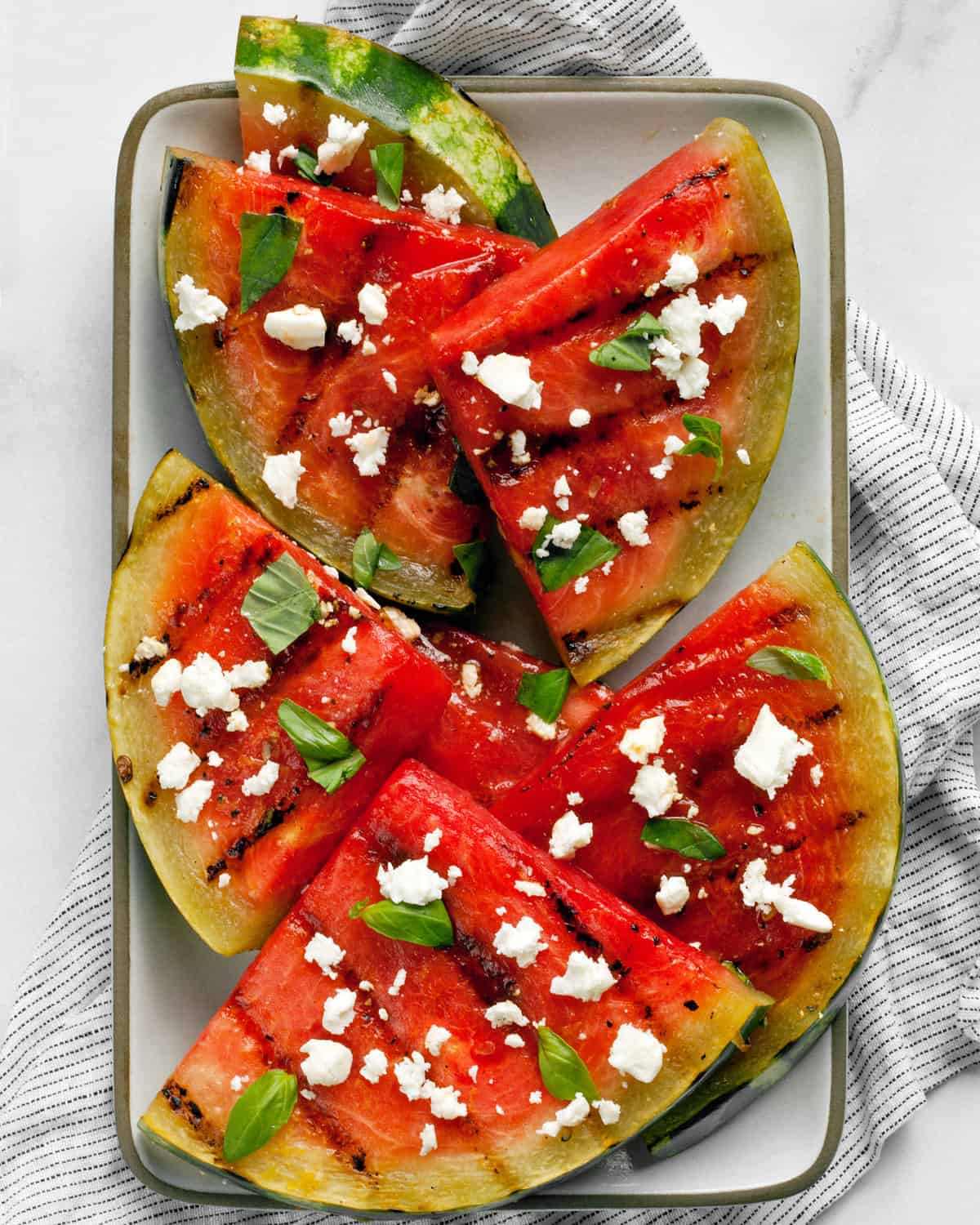 Grilled watermelon wedges with feta and basil on a plate.