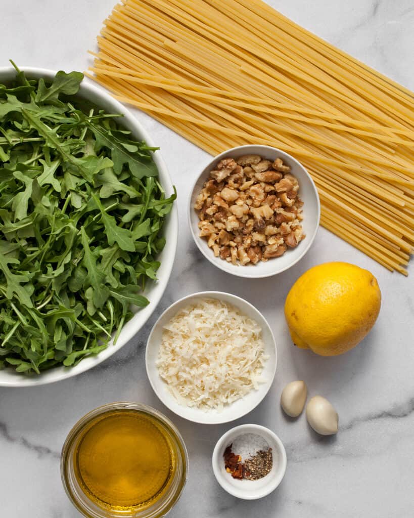 Ingredients including pasta, arugula, lemon, garlic, olive oil and walnuts.
