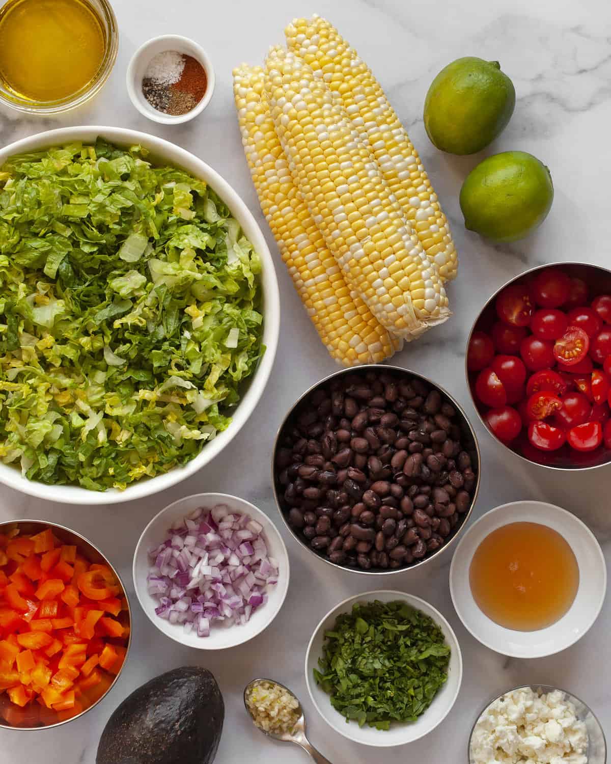 Ingredients including romaine, corn, black beans, tomatoes, peppers, onions, limes, tomatoes, oil and spices.