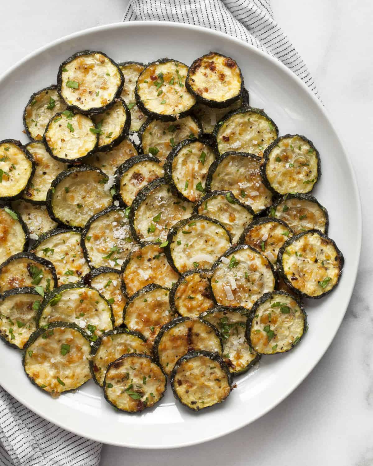 Roasted zucchini on a plate sprinkled with chopped parsley.