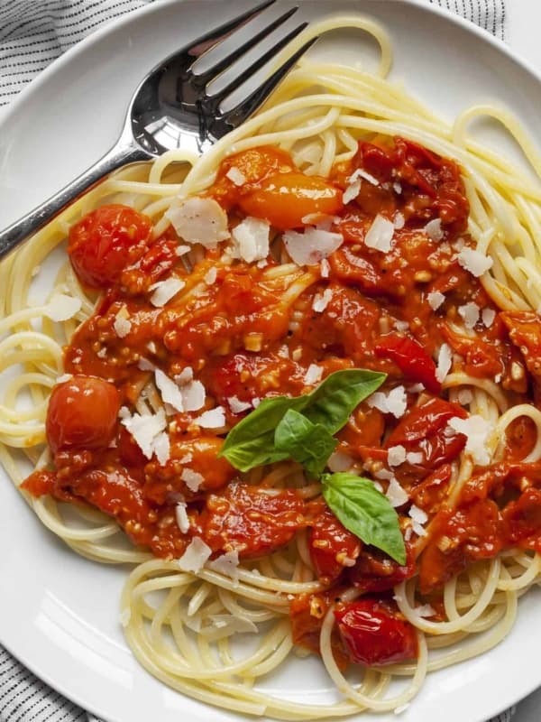 Tomato sauce spooned over spaghetti and topped with Parmesan and fresh basil leaves.