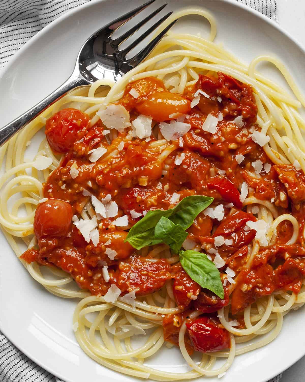 Tomato sauce spooned over spaghetti and topped with Parmesan and fresh basil leaves.