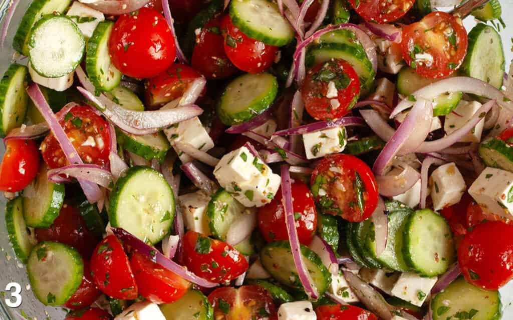 Close-up image of salad ingredients and vinaigrette stirred together.