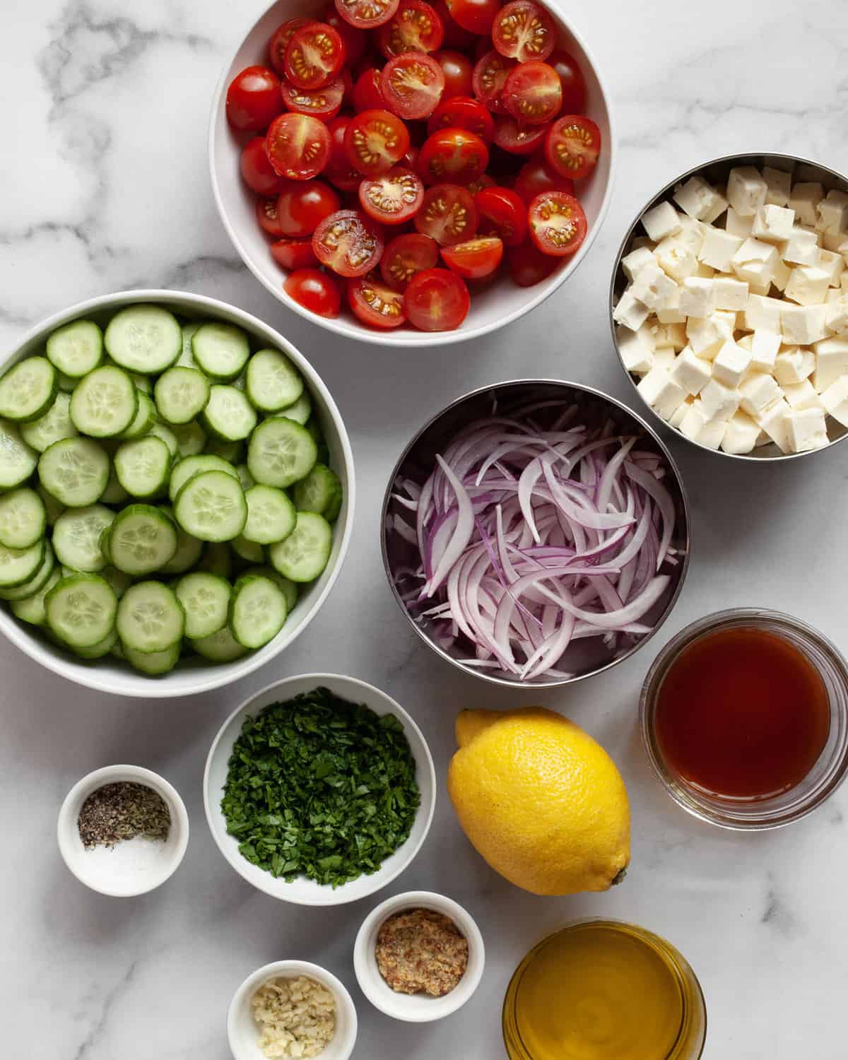 Ingredients including cucumbers, tomatoes, red onions. feta, parsley, lemon, olive oil, spices and garlic.