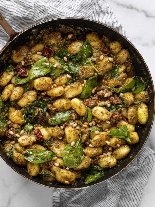 A large skillet with gnocchi, sun dried tomatoes and spinach simmered in pesto and fresh lemon juice.