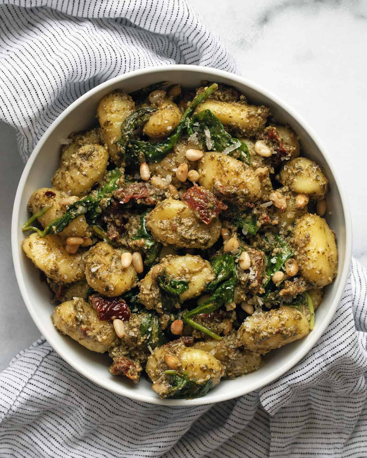 Pesto gnocchi with sun dried tomatoes, spinach and pesto in a small bowl.