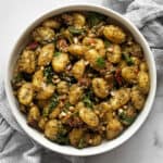 Gnocchi with pesto, sun-dried tomatoes an spinach in a bowl.