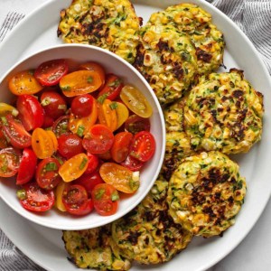 Zucchini corn fritters on a plate with a tomato salad.