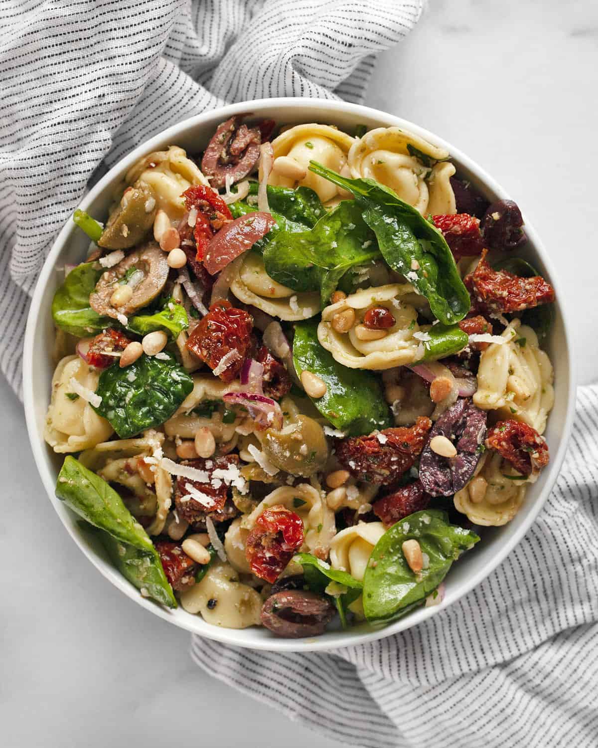 Pasta salad with sun dried tomatoes, olives and spinach in a small bowl.