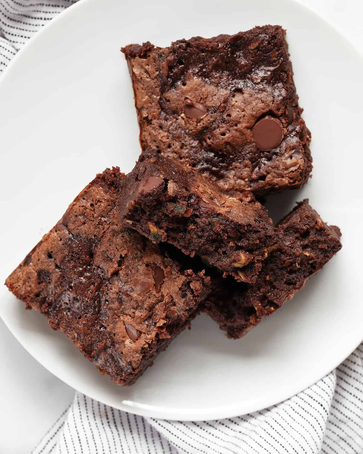 Three zucchini brownies on a plate with one broken in half.