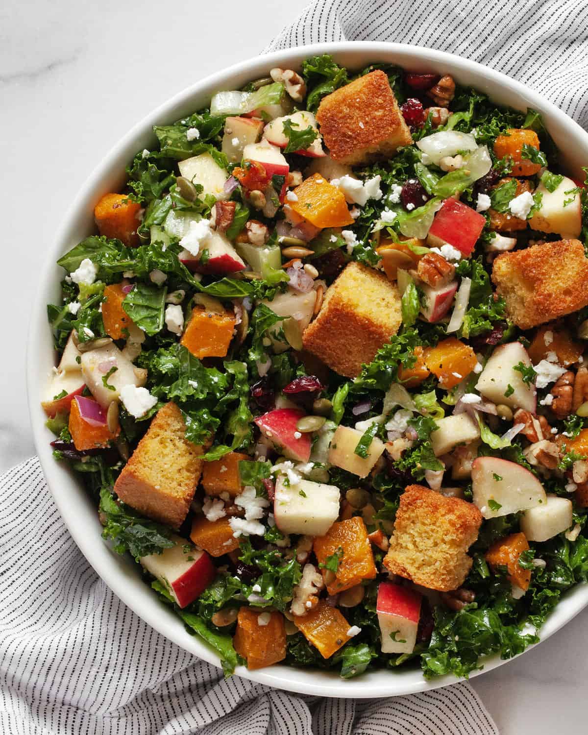 Salad with roasted butternut squash, apples, kale and romaine in a bowl.
