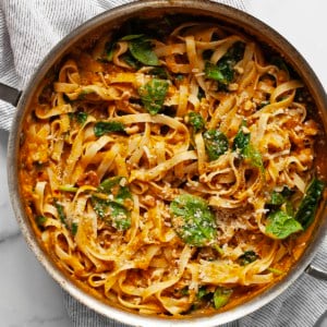 Pasta with pumpkin sauce, spinach, walnuts and parmesan in a pan.