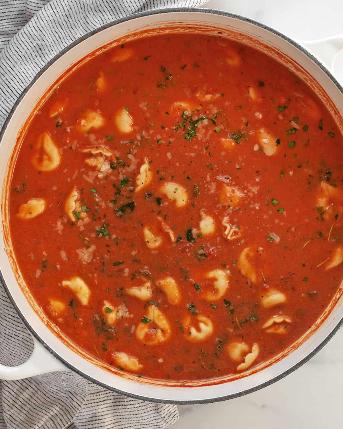 Large pot of creamy tomato soup with tortellini and kale.