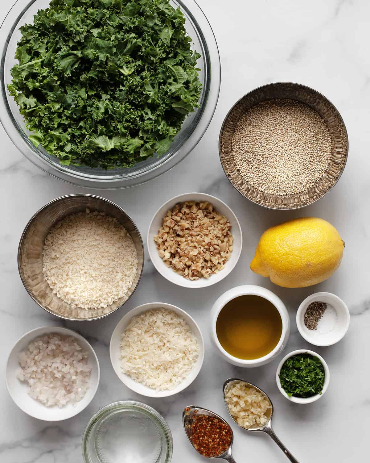 Salad ingredients including quinoa, kale, lemon, breadcrumbs, walnuts, parmesan, garlic, mustard, shallots, olive oil, salt and pepper.
