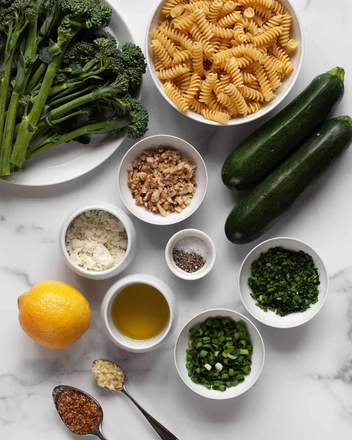 Ingredients including broccolini, zucchini, pasta, lemon, walnuts, lemon, olive oil, feta, salt and pepper.