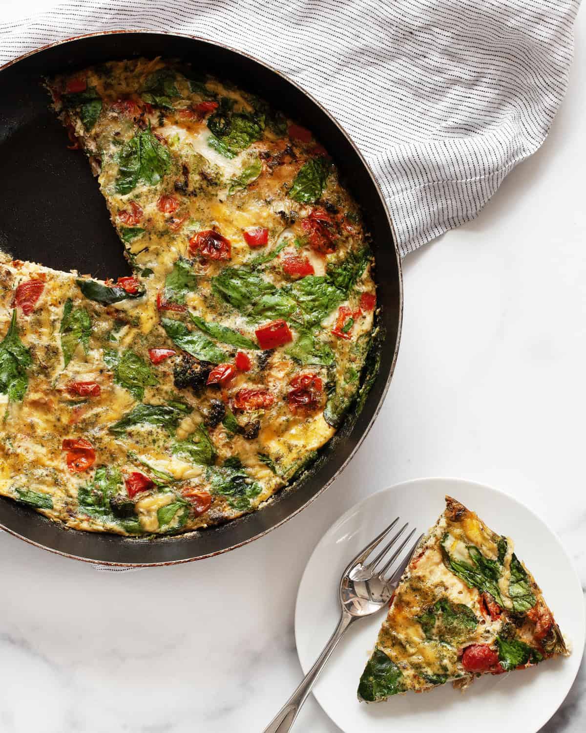 Roasted vegetable frittata in a skillet with a slice on a plate.