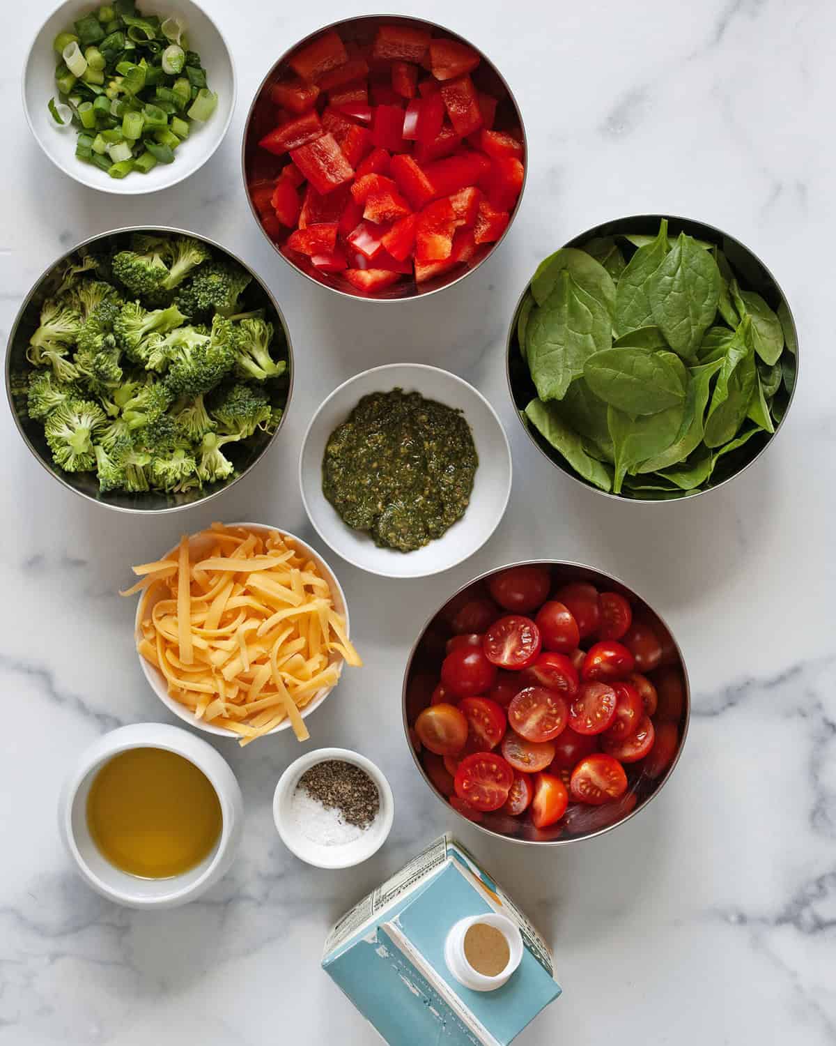 Ingredients including egg whites, tomatoes, red peppers, broccoli, cheddar, spinach, pesto, oil, scallions, salt and pepper.