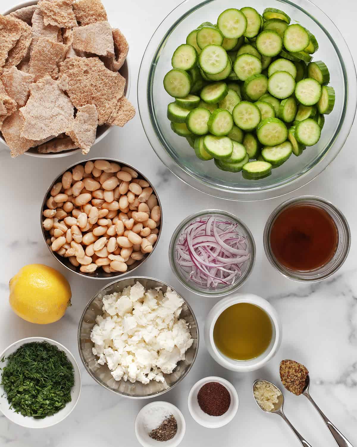 Ingredients including sliced cucumbers, red onions, feta, torn pita, fresh herbs. lemon, garlic, mustard, olive oil and red wine vinegar.