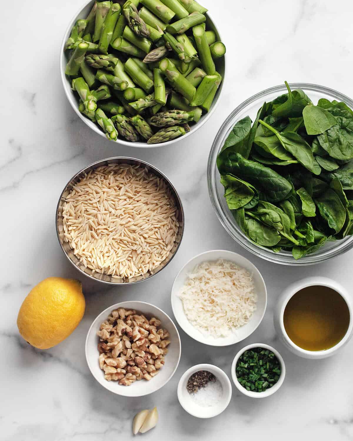 Ingredients for pesto orzo including spinach, lemon, orzo pasta, asparagus, parmesan, olive oil, chives, walnuts, salt and pepper.