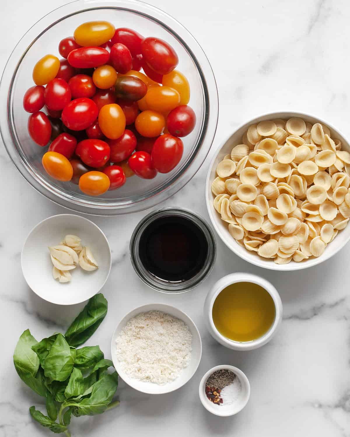 Ingredients including cherry tomatoes, olive oil, garlic, orecchiette, balsamic vinegar, parmesan, basil and seasonings.