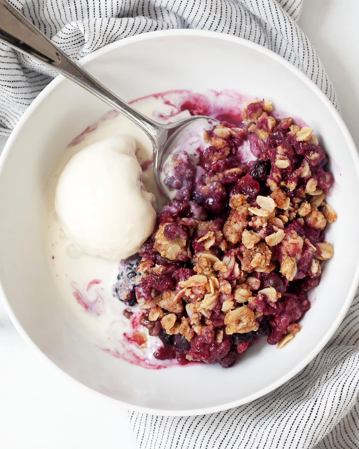 Mixed berry crumble in a serving bowl with a scoop of ice cream.