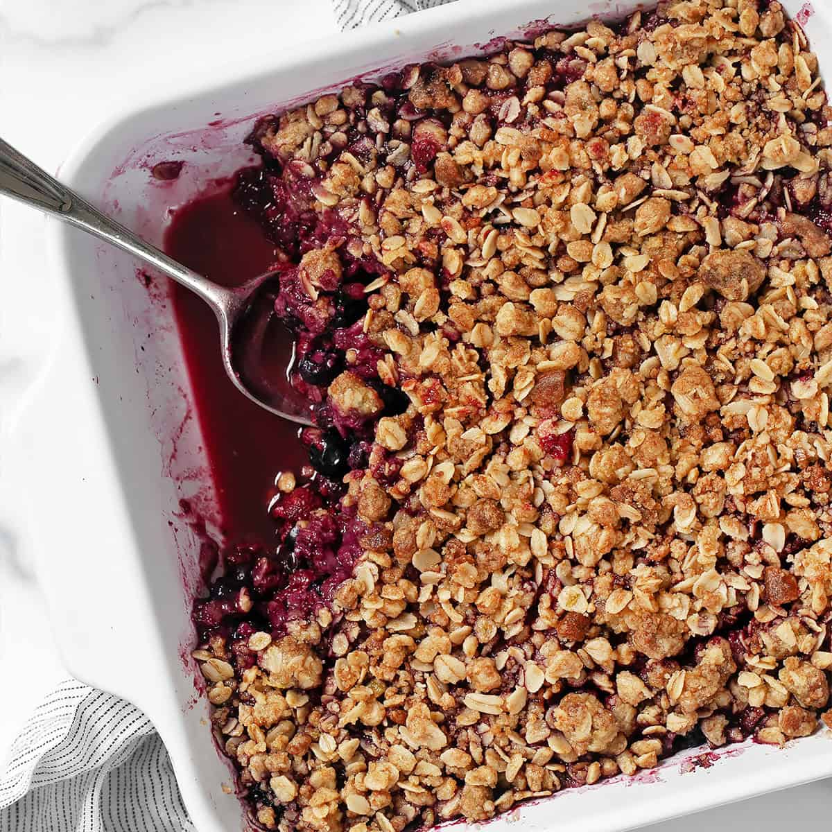Mixed berry crumble in a dish with a spoon.