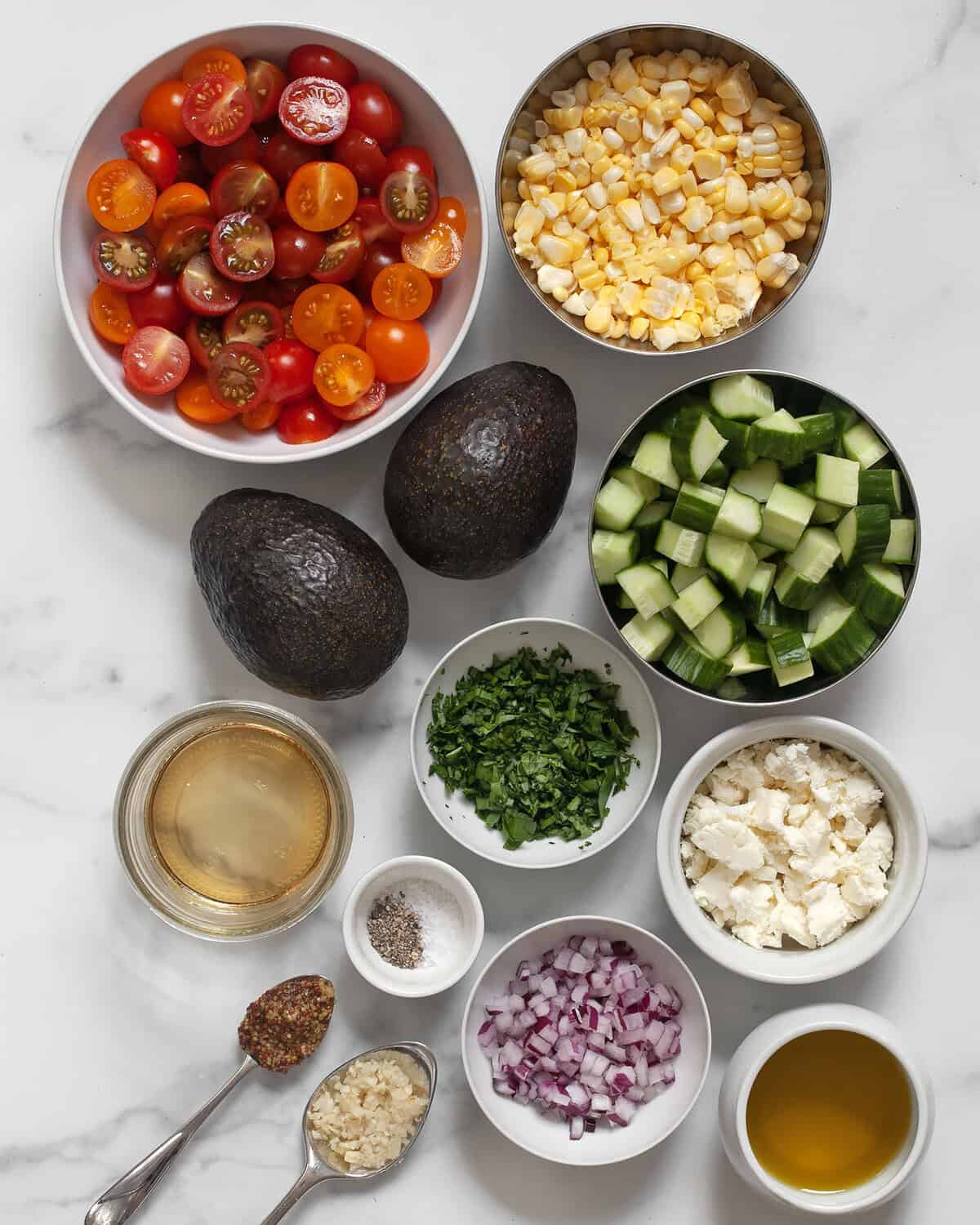 Ingredients including two avocados, tomatoes, cucumbers, corn, fresh herbs, feta, white balsamic vinegar, garlic, mustard, vinegar, red onions and oil.